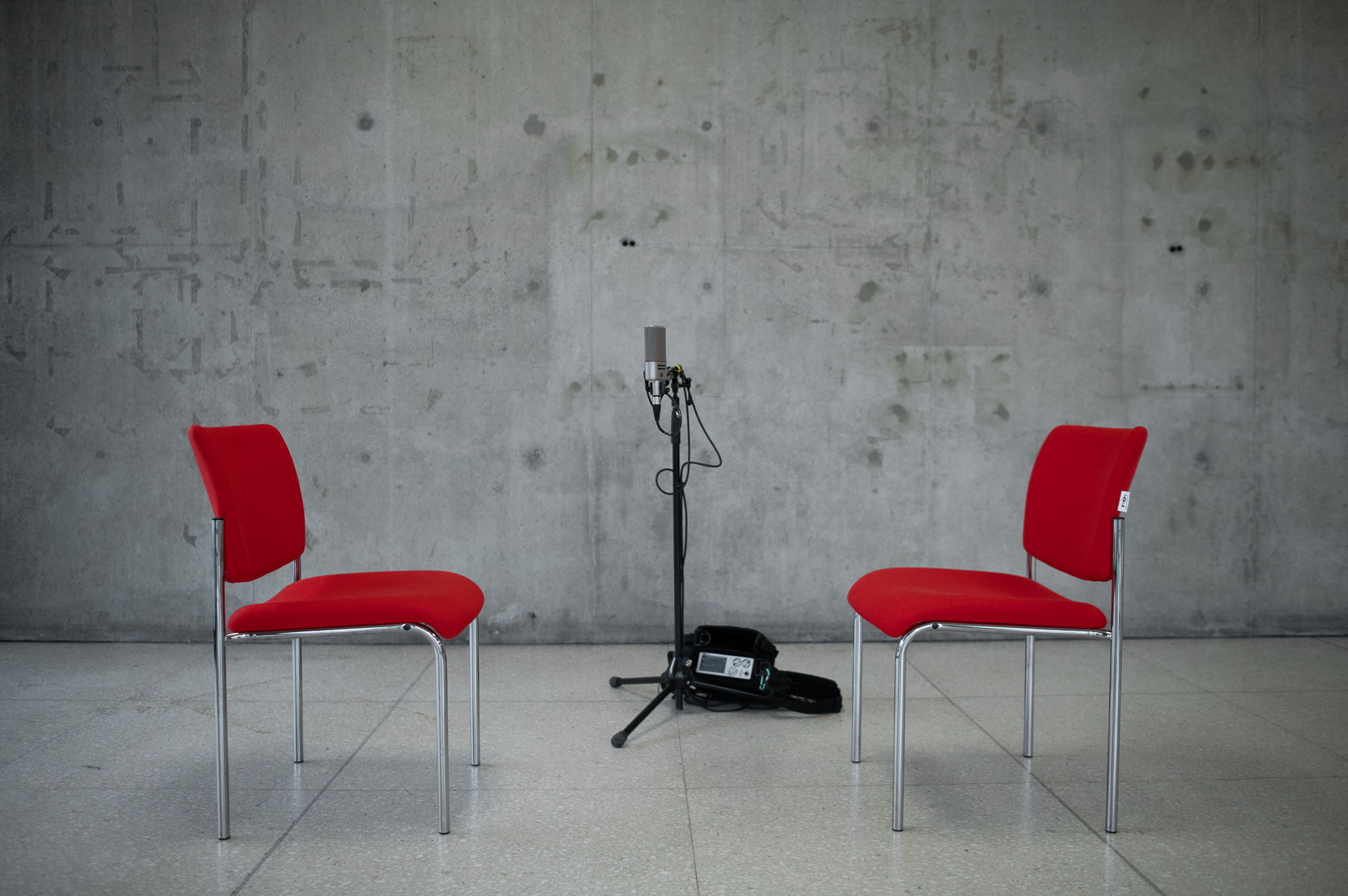 Zwei rot bezogene Sessel stehen einander gegenüber, dazwischen befinden sich ein Mikrofon auf einem Stativ und ein Aufnahmegerät.